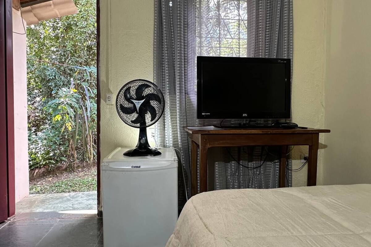 A room with a bed, a small table with a television, a fan, and a washing machine.