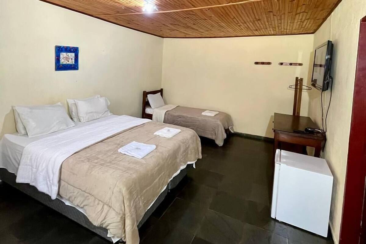 A room with two beds, a small table, and a white appliance, likely a refrigerator.