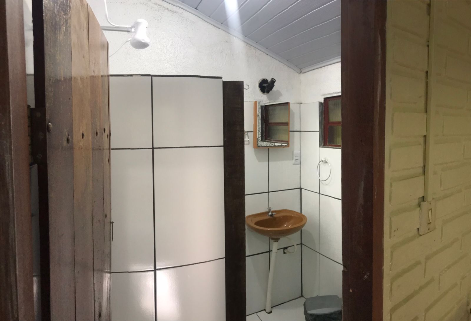 A small bathroom with white tiled walls, a wooden door, a single sink, and a mirror.