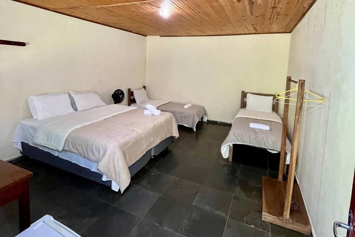 A bedroom with a wooden ceiling, two single beds, a bedside table, and a small desk.
