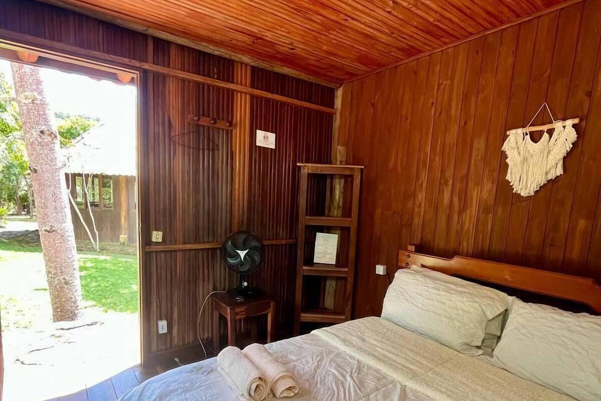 A wooden room with a bed, a fan, and a small table.
