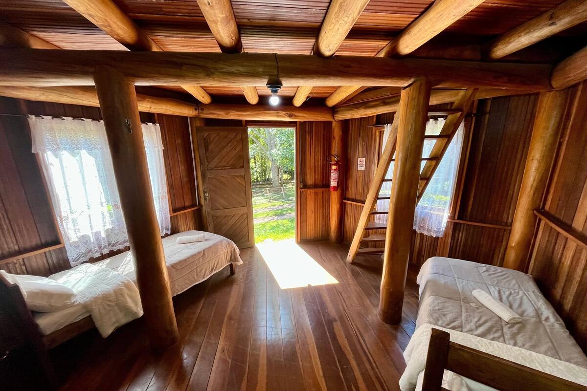 A rustic wooden cabin with two beds, a wooden ceiling, and a view of the outdoors.