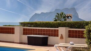 Un espace piscine avec vue sur les montagnes, une poubelle et une table avec un chapeau.