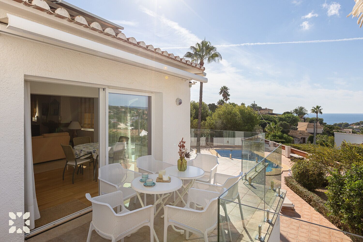 Ein Balkon mit Glastisch und Stühlen, ein Pool und Meerblick.