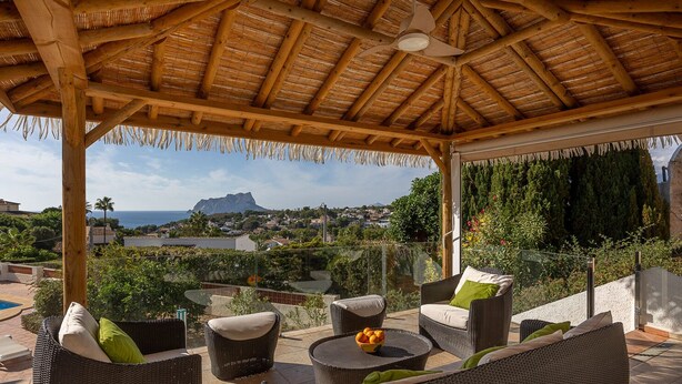 Un espace extérieur aménagé, abrité et doté de mobilier en osier, offrant une vue sur la mer et les montagnes.