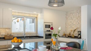 Une cuisine moderne avec un coin repas, comprenant une table en verre, un saladier rempli d’oranges et un vase avec des fleurs.