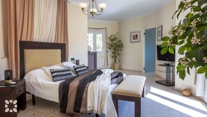 Ein Schlafzimmer mit einem großen Bett, einem Nachttisch, einer Bank, einem Fernseher und einer Topfpflanze.