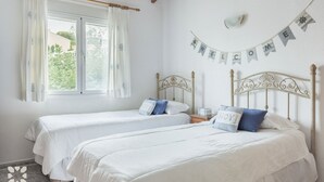 Ein Zimmer mit zwei Einzelbetten, einem fenster mit Vorhängen, einer Wanduhr und einem Willkommensspruch.
