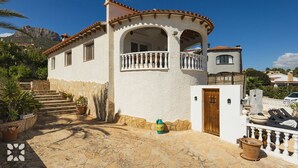 Ein zweistöckiges Haus mit weißer Fassade und Terrakotta-Dachziegeln. Es verfügt über einen Balkon mit weißen Brüstungen und einer Steintreppe, die zum Eingang führt.