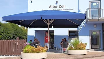Een gebouw met een bord waarop 'Alter Zoll' staat en terrasmeubilair met parasols.