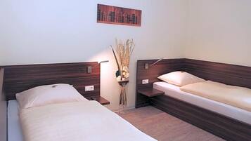 A room with two beds, a nightstand, a wall-mounted lamp, and a decorative vase.
