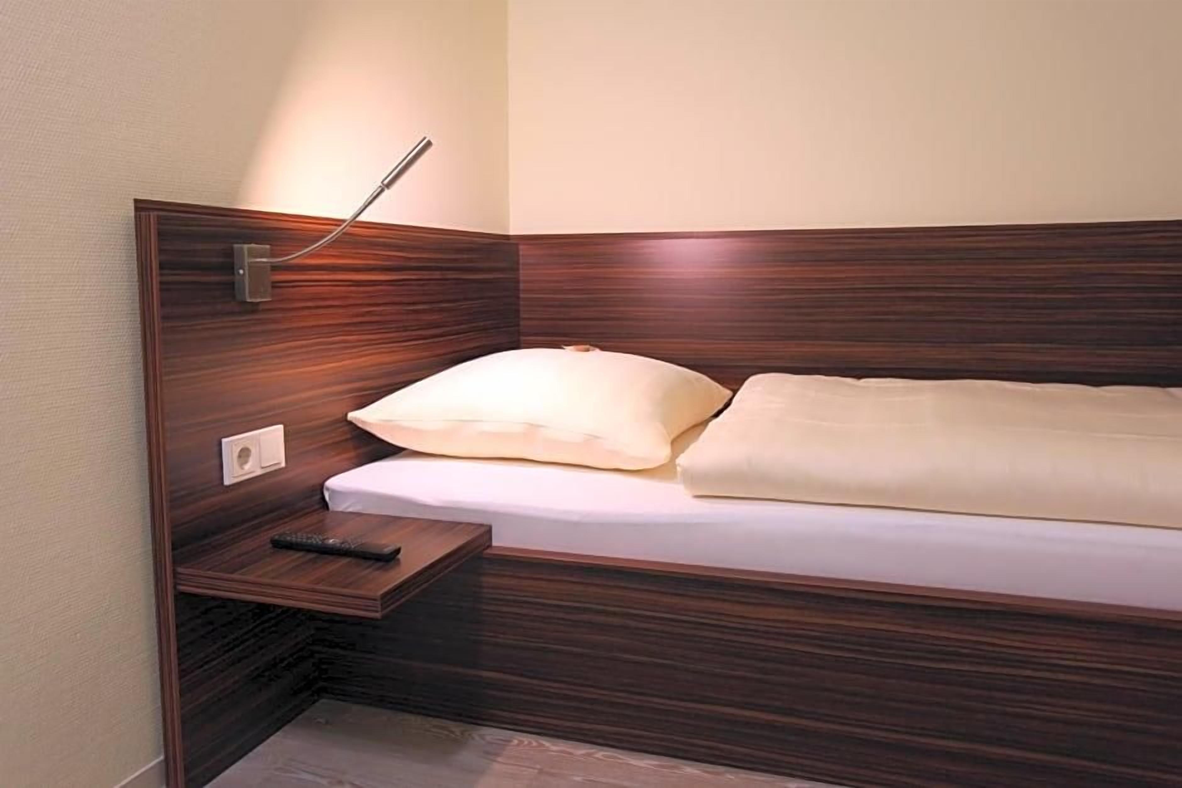 Een enkel bed met een houten hoofdbord, een nachtkastje en een afstandsbediening erop.