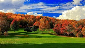 Ein Golfplatz mit Herbstlaub, ein Clubhaus und ein klarer, blauer Himmel.