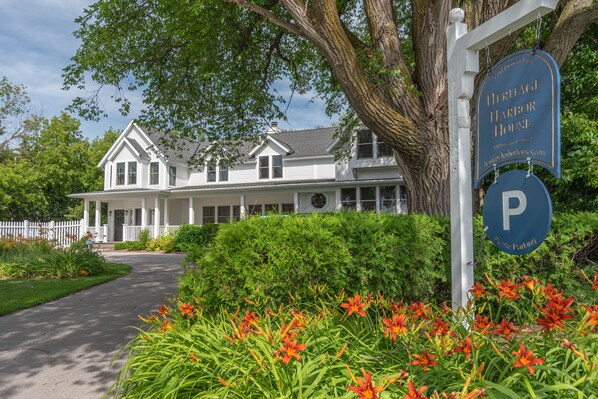 A white heritage house with a porch, surrounded by greenery and orange flowers.