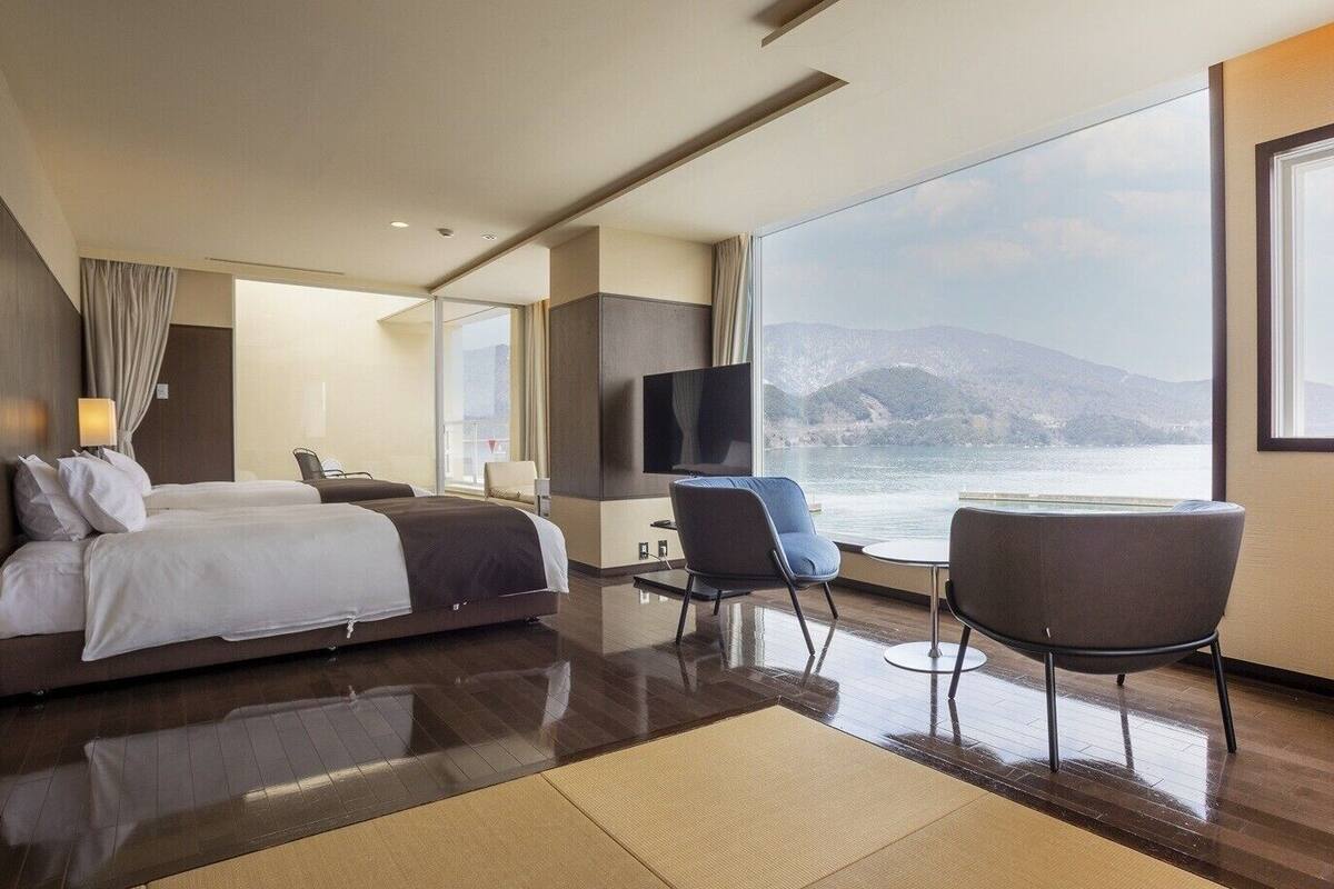 A modern hotel room with a large bed, a TV, a seating area with a view of the sea, and a large window.
