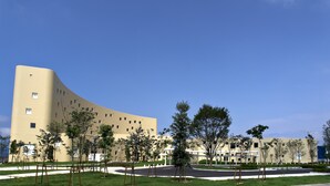 A modern building with a curved facade, surrounded by a well-maintained lawn and young trees.