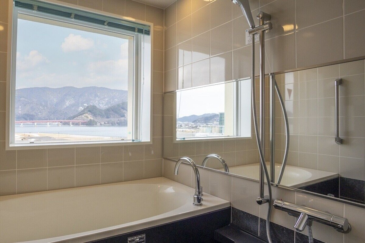 Un baño moderno con bañera, ducha, un ventanal grande y vistas a montañas.