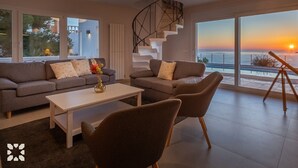 A modern living room with a sofa, chairs, a coffee table, and a view of the sunset over the ocean. - Villa LIGHTHOUSE by Abahana Villas (Benitachell)