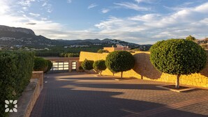A courtyard with a paved walkway, stone walls, and neatly trimmed trees. - Villa HAPPY FAMILY by Abahana Villas (Calpe)