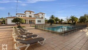 A poolside area with lounge chairs, a swimming pool, and a building with a tiled roof and multiple windows. - Villa HAPPY FAMILY by Abahana Villas (Calpe)
