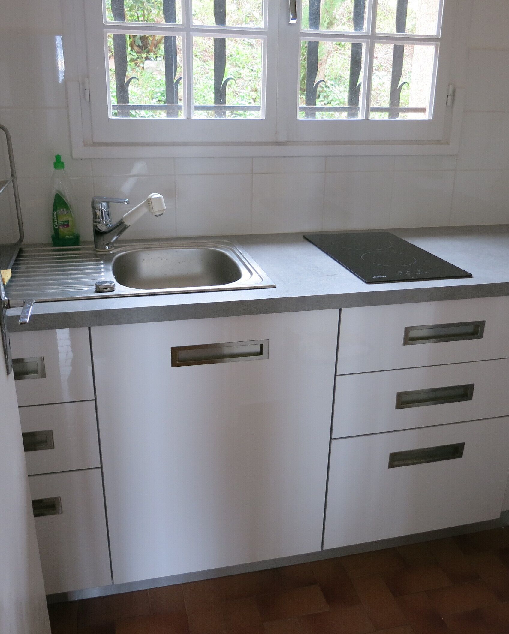 Een keuken met een roestvrijstalen spoelbak, een inbouwfornuis en witte kastjes met zilverkleurige handgrepen.