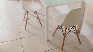 Une petite pièce propre, avec une table blanche, deux chaises blanches, un meuble blanc et une étagère blanche sur laquelle se trouve une machine à café.