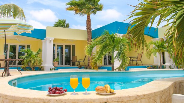 Un espace aménagé au bord de la piscine, comprenant une table à manger, des chaises, un palmier et un bâtiment aux murs bleus et jaunes.