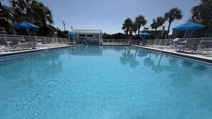 A rectangular swimming pool with clear blue water, surrounded by white lounge chairs and blue umbrellas. - Sundown B 13 (Pensacola)