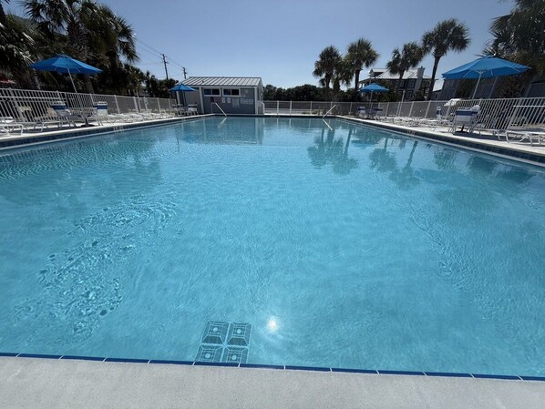 A clear swimming pool with a lifeguard stand, lounge chairs, and umbrellas.