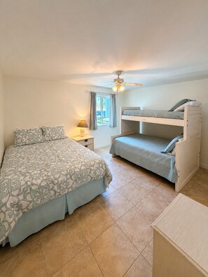 A bedroom with a bed, a desk, a ceiling fan, and a window.