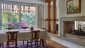 Comedor con mesa dispuesta para cuatro, chimenea y vista a zonas verdes.