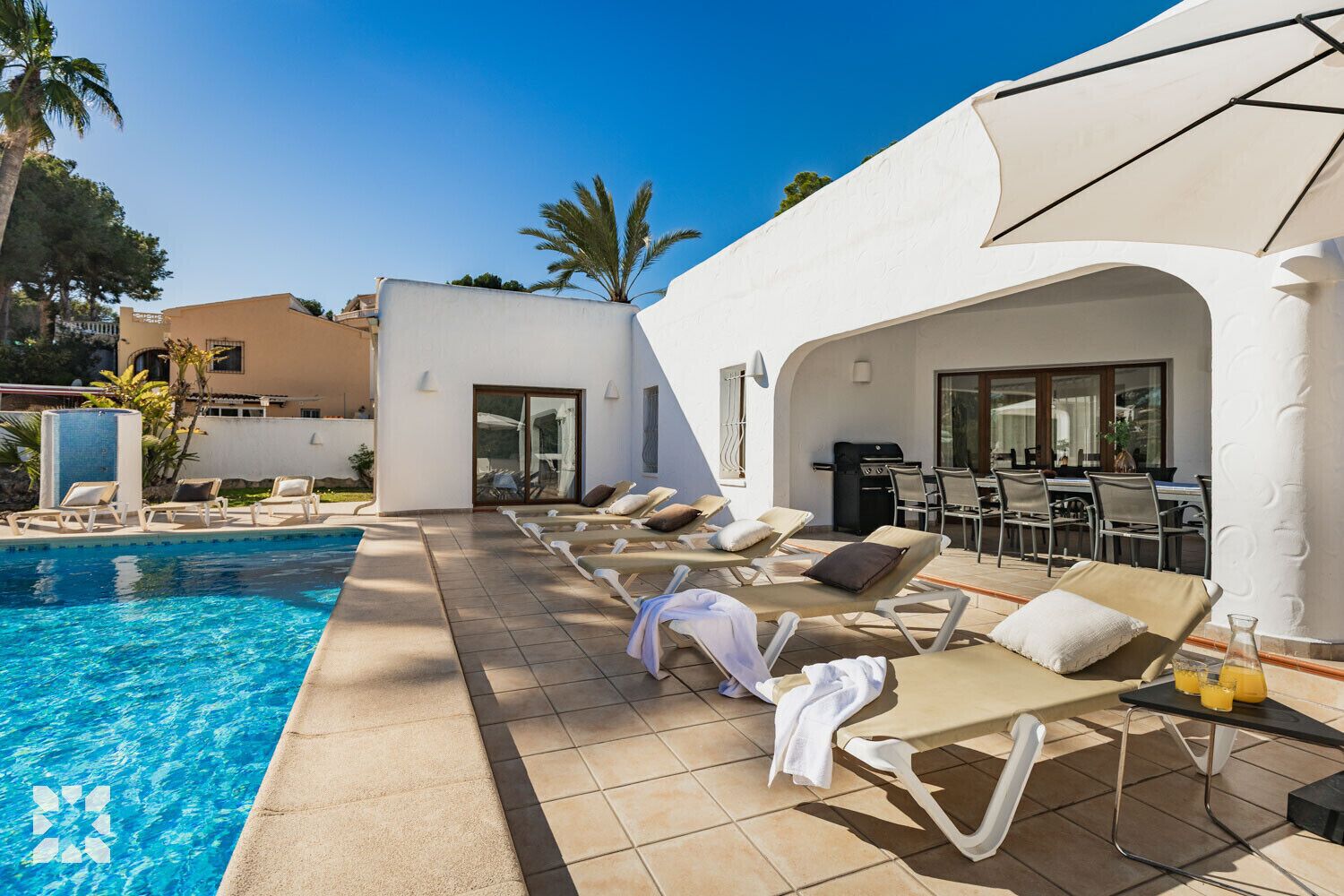 A poolside area with lounge chairs, a barbecue grill, and a dining table.
