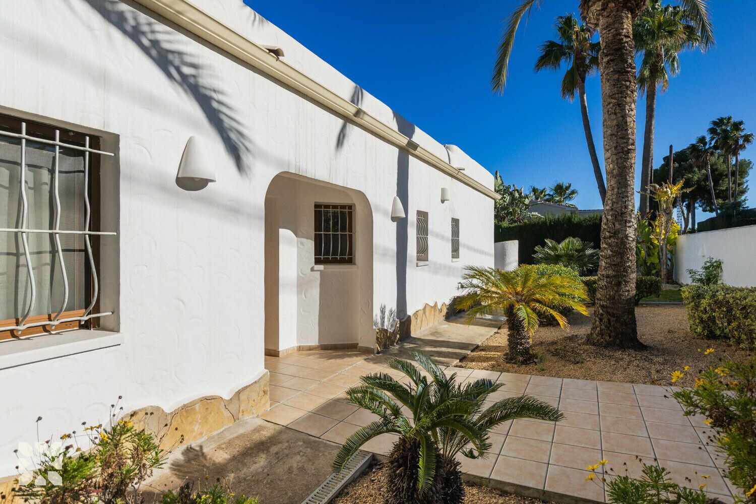 A white building with a tiled patio, palm trees, and a clear blue sky.