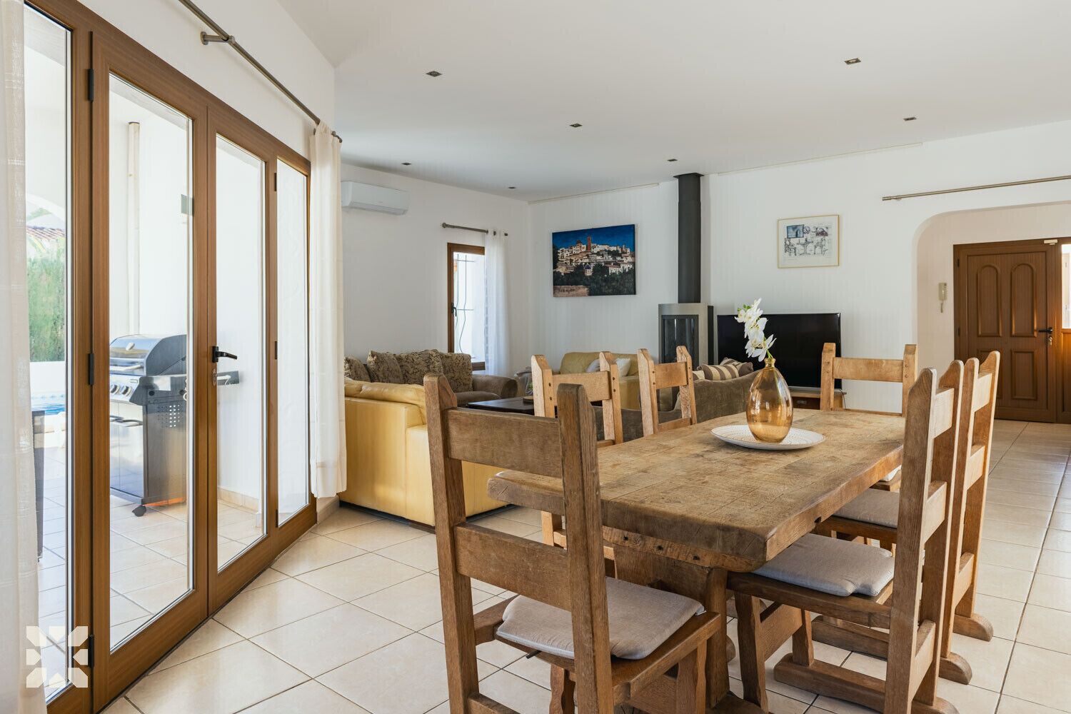 Un espace repas comprenant une table et des chaises en bois, un canapé, une cheminée et une grande fenêtre donnant sur un beau paysage.