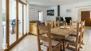 Een eetgedeelte met een houten tafel en stoelen, een bank, een open haard en een groot raam met uitzicht.