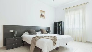Een slaapkamer met een bed, nachtkastjes, een lamp, een lijst aan de muur en een raam met gordijnen.