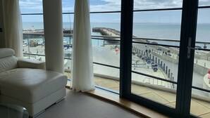 A room with large windows overlooking a beach and pier, a white sofa, and a glass table. - Beachside, stunning apartment with sea and harbour views (West Bay, Bridport)