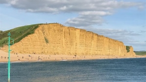 A coastal scene with a large cliff and a sandy beach. - Beachside, stunning apartment with sea and harbour views (West Bay, Bridport)