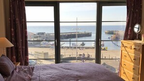 A bedroom with a large window offering a view of the beach and sea. - Beachside, stunning apartment with sea and harbour views (West Bay, Bridport)