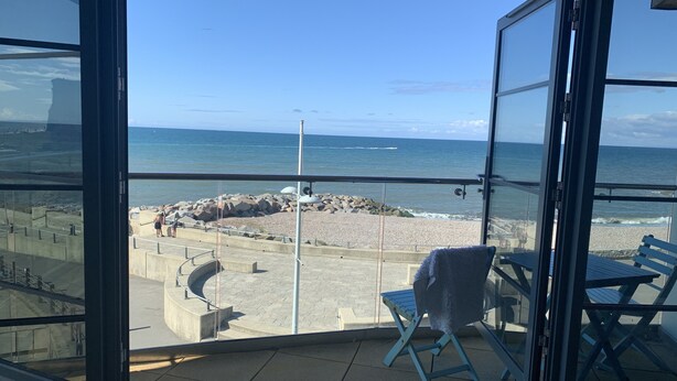 A balcony with a view of the beach, a chair, and a table. - Beachside, stunning apartment with sea and harbour views (West Bay, Bridport)