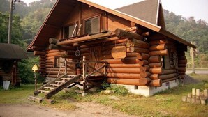 Una cabaña de troncos con una escalera empinada que lleva a la entrada, rodeada de troncos y construcciones de madera.