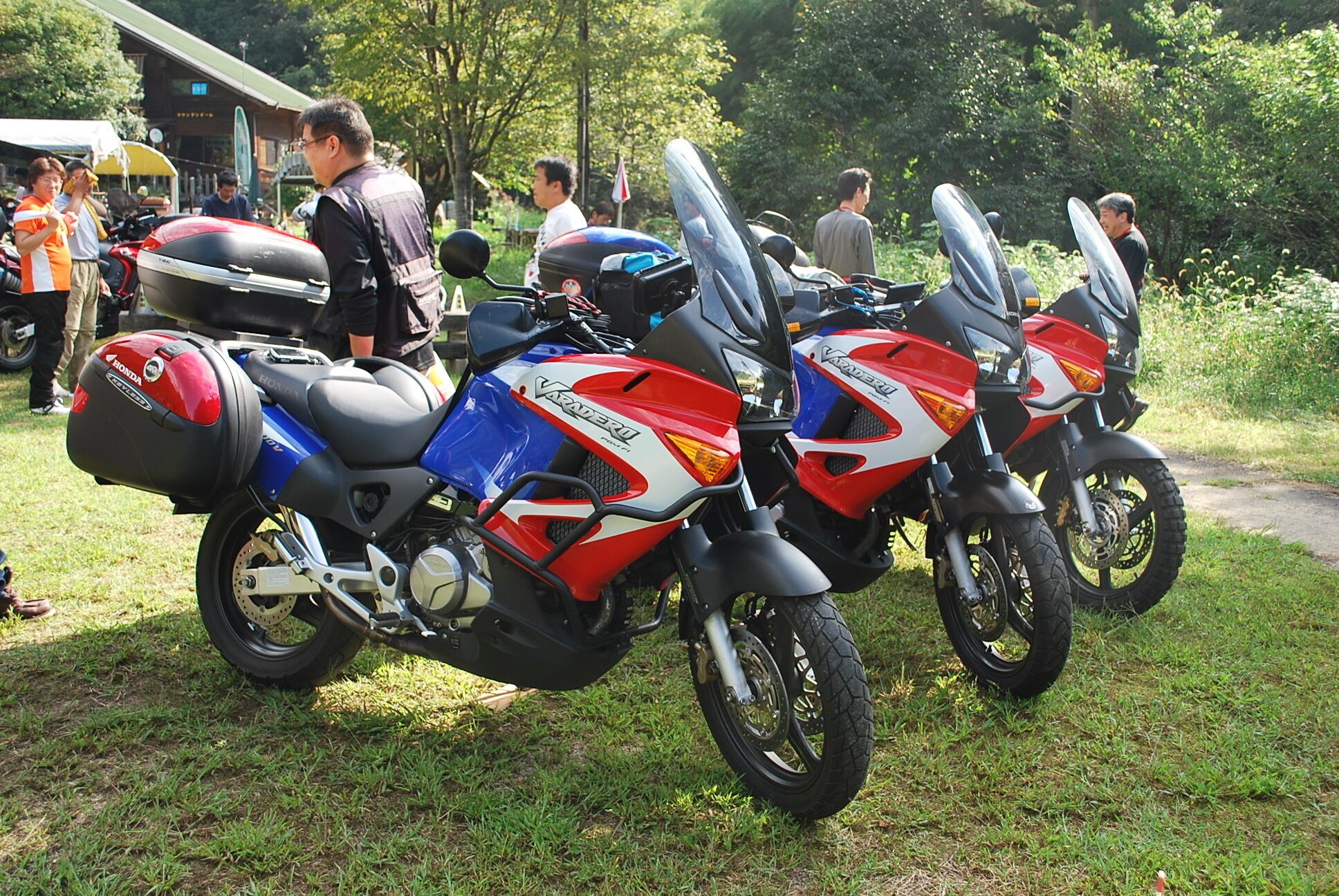 Two motorcycles parked on grass with a crowd in the background.