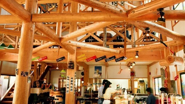 Un interior rústico de madera con vigas a la vista, mesas de madera y una zona de bar.