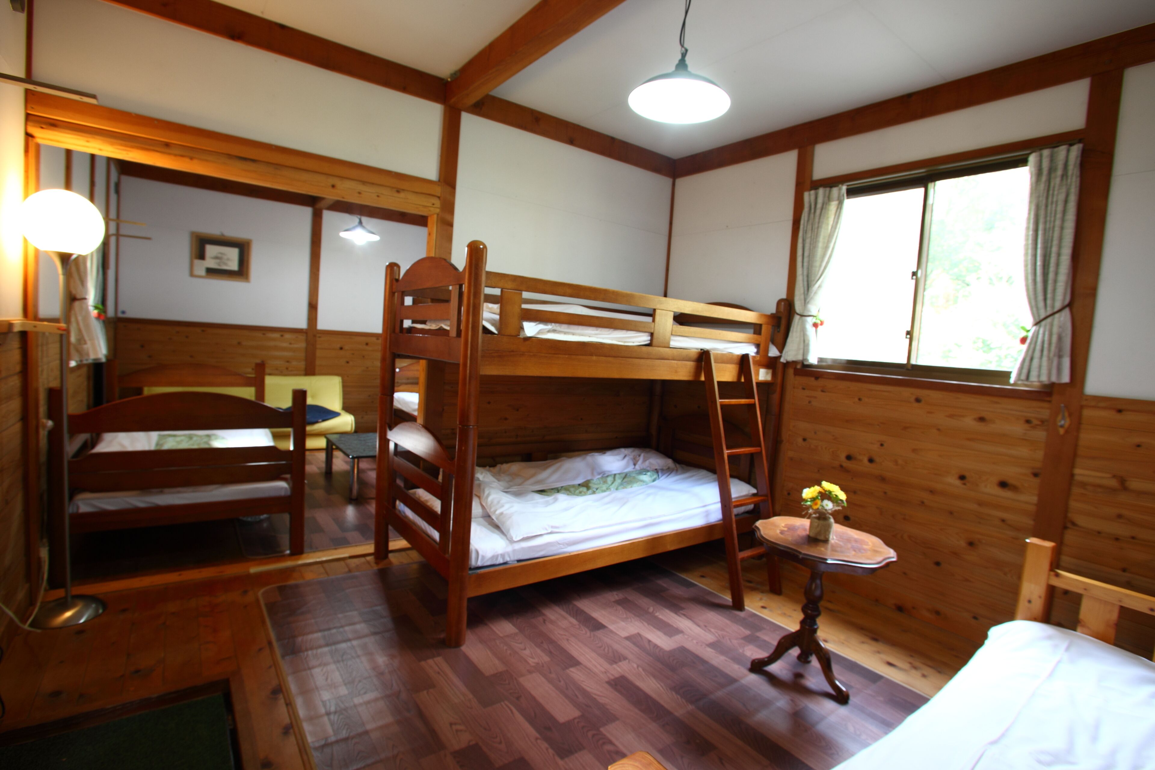 Una cabaña de madera con literas, una pequeña mesa con flores y una ventana con cortinas.