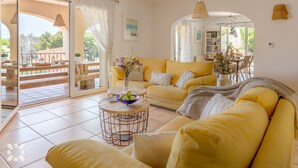Ein helles Wohnzimmer mit gelben Sofas, einem Couchtisch mit Blumenvase und einem Balkon mit Gartenmöbeln.