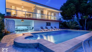Una casa de dos pisos con piscina, mobiliario exterior y un interior bien iluminado.