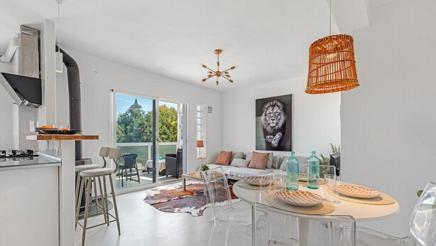 Una cocina moderna con estufa a gas, un comedor con mesa redonda y una sala de estar con sofá y ventana grande.