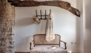 Un interior rústico con pared de piedra, viga de madera, una silla tejida y un perchero de pared con un sombrero y una bufanda.