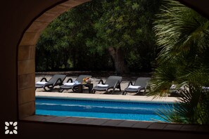 Zona de piscina con sillones reclinables y una mesa con una cesta de frutas.
