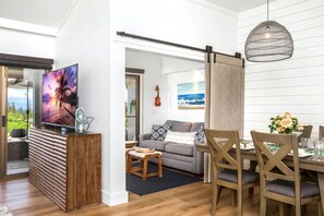 Ein modernes Wohnzimmer mit Fernseher, einem Essbereich mit Holzstühlen und Blick ins Freie.